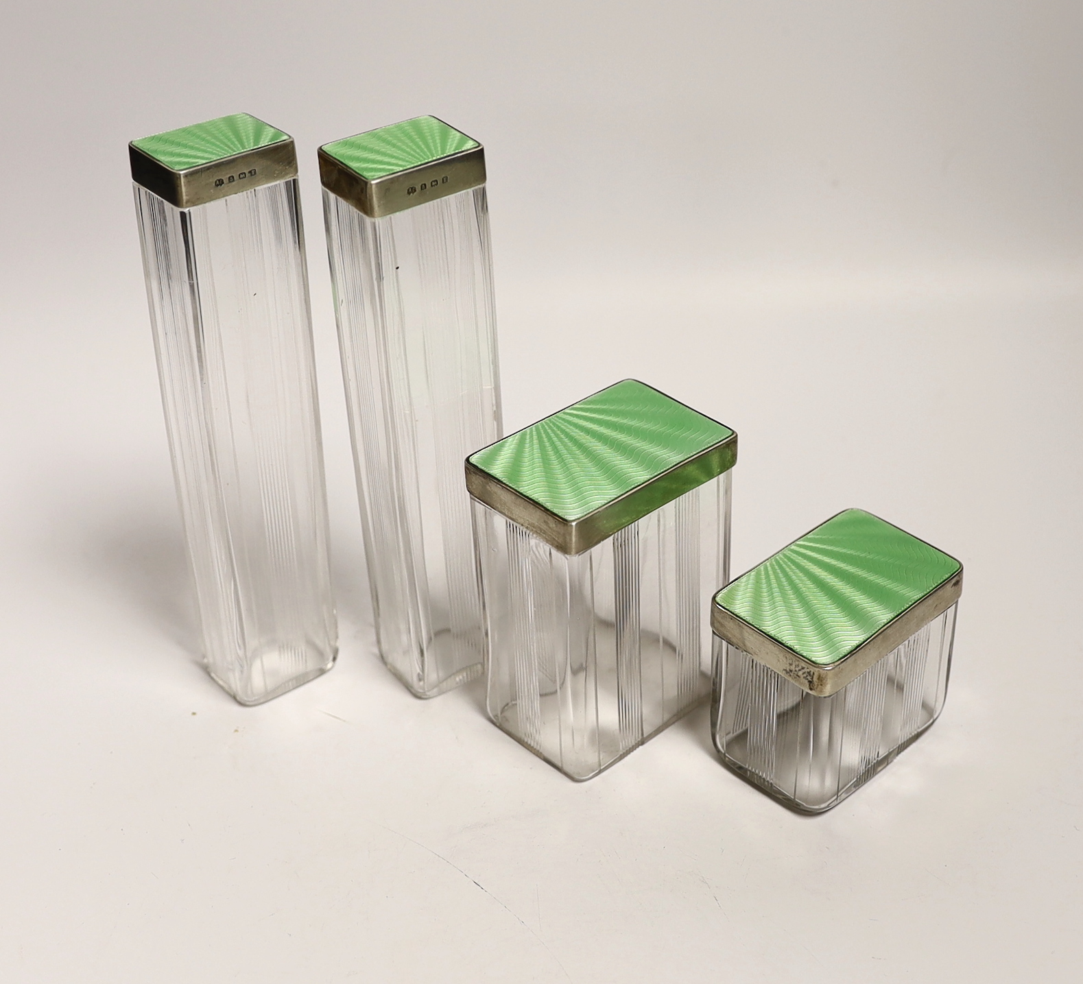 Four George VI silver and green guilloche enamel lidded glass toilet jars, Alexander Clark Co. Birmingham, 1943, tallest 16.2cm.